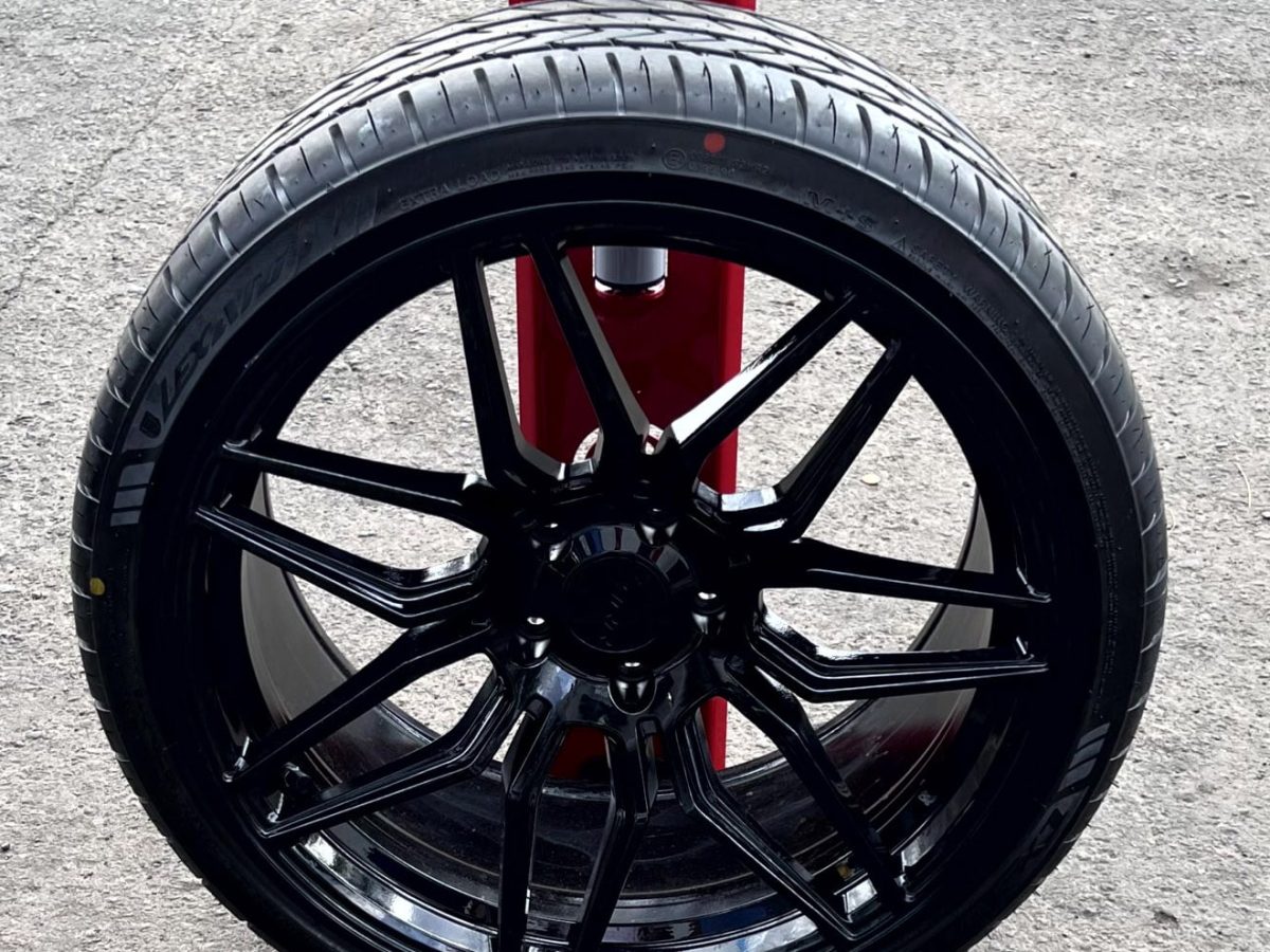 Gloss-black multi-spoke alloy wheel with its tire mounted, standing on a wheel stand