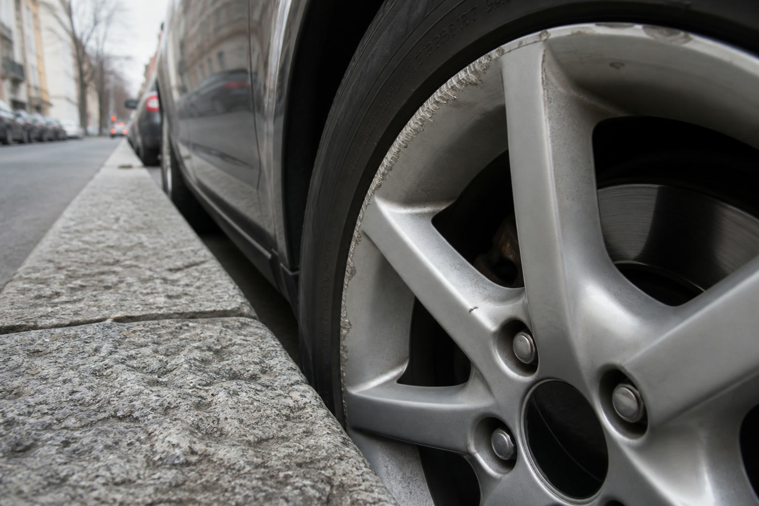 Close-up of an alloy wheel with scraped curb rash on a car parked against a granite curb