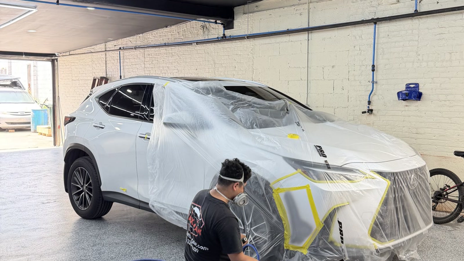 Waxman technician spraying a masked Lexus SUV in the Jersey City repair bay