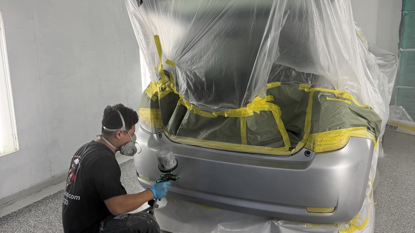 Waxman technician spraying a masked rear bumper inside the Jersey City paint booth
