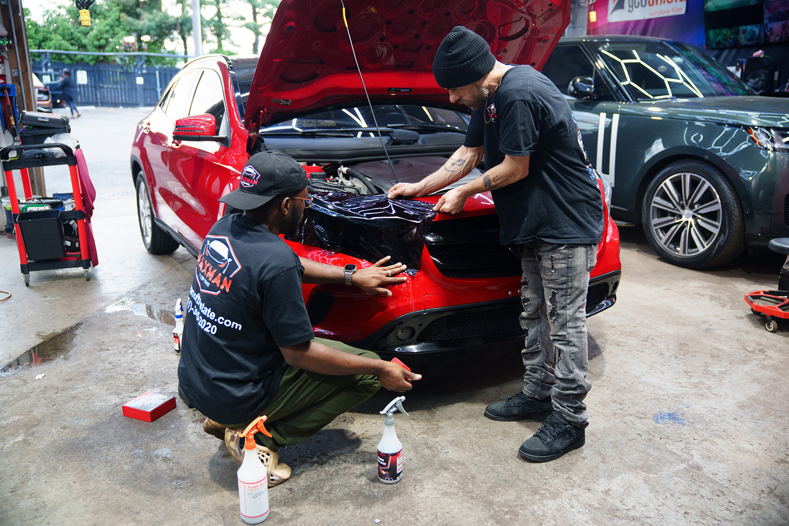 Waxman technicians wrapping the front end of a red Mercedes GLE in protective film