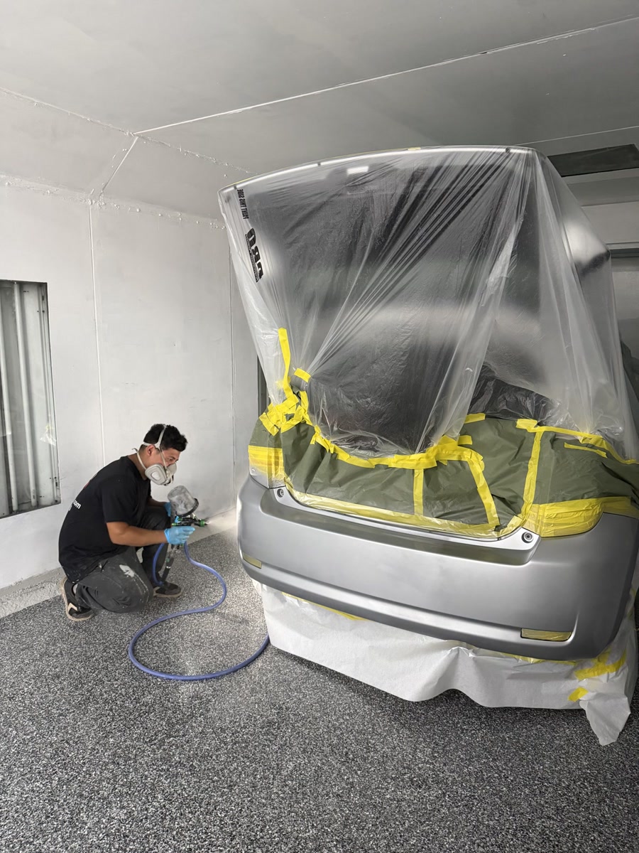 Waxman technician in a respirator spraying sealer onto a masked vehicle in the paint booth