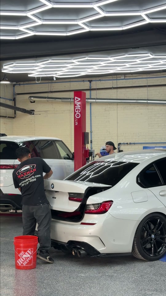 Waxman technician working on a white BMW under the hexagon lights of the Jersey City repair bay